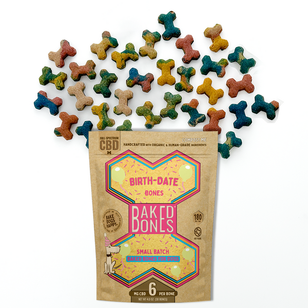 Baked dog bones of varying colors (red, blue, green, yellow, mixed) spilling out of a Kraft BakedBones bag with a pink/yellow/blue bone and “BIRTH-DATE BONES” on the front